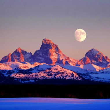 Tetons Tetons 'ta gün batımı ışığı parlıyor. Tetons dağları, ay yükselirken engebeli.
