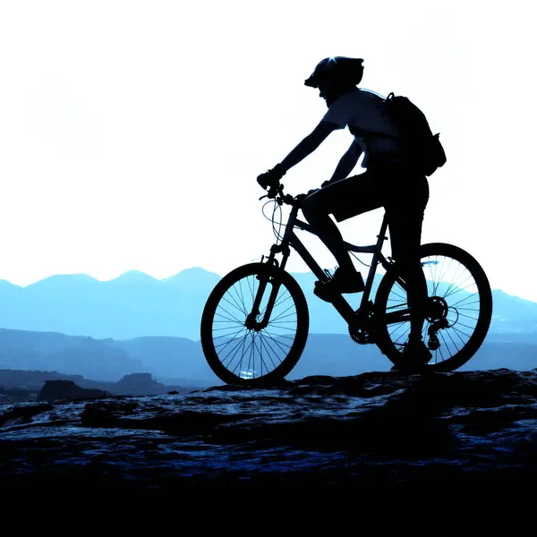 Mountain biking up a trail in the mountains rider silhouette silhouetted on ridge