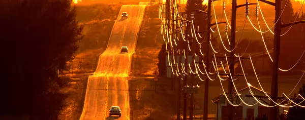 Autos Fahren Auf Alter Landstraße Bei Sonnenuntergang Der Hochspannungsleitungen lizenzfreie Stockbilder