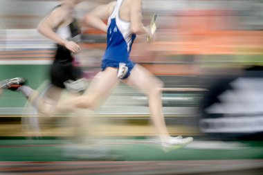 Yarış pisti etrafında koşan bir koşucu sopa rölesiyle takım çalışmasını ve yarışmasını temsil ediyor.