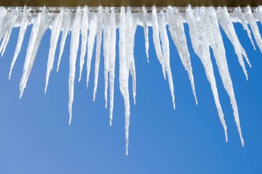 Evin çatısından sarkan buz sarkıtları eriyen buzlar ve açık mavi gökyüzü