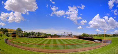 Manicured mowed grass lines on a baseball field diamond with blue sky and clouds summer day