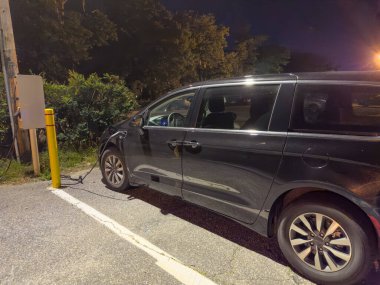 Siyah minivan eklenti hibrit araç gece bir istasyonda şarj