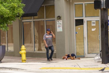 Miami, FL, ABD - 25 Eylül 2024: Miami 'de evsiz bir kadının yanından geçen insanlar