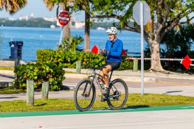 Key Biscayne Miami, FL, ABD - 8 Mart 2025: Son sınıf öğrencisi akıllı telefonuyla mesajlaşırken bisiklete biniyor