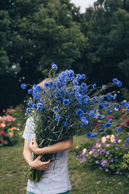 Bir yaz bahçesinde elinde büyük bir buket çiçek tutan bir çocuk.