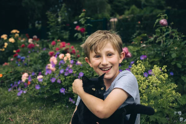 快乐的男孩在夏天的花园里带着一只黑猫 — 图库照片