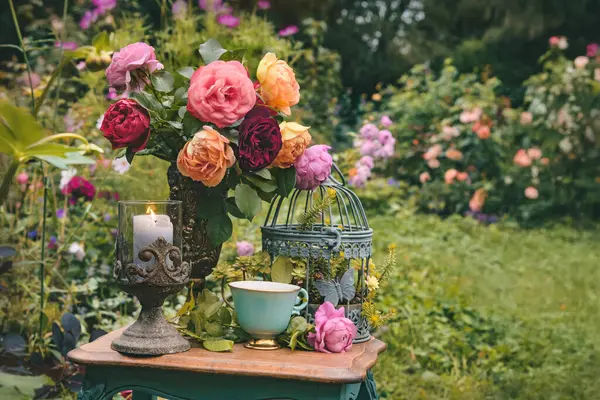 Vazoda bir buket pembe ve kırmızı gül ve masada bir yaz bahçesinde bir fincan çay. Romantik yaz, bahçede çiçeklerle dolu bir hayat.