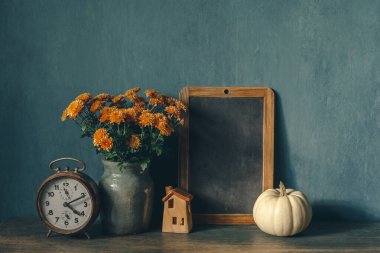 Mutfakta antika bir çalar saat, siyah bir karatahta, bir buket kasımpatı ve mumlu dekoratif bir balkabağı ile sonbahar modeli. Şükran Günü için klasik kırsal tarzda rahat ev dekorasyonu kavramı 