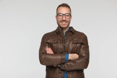 çekici sıradan bir adam kollarını kavuşturuyor, gözlük takıyor ve gri arka planda kameraya gülümsüyor.