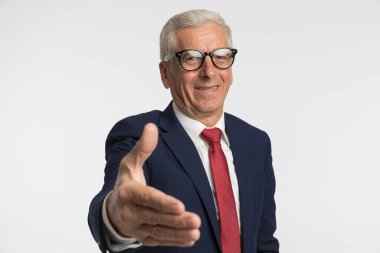 İş adamı elini sıkmak, dostça davranmak ve gri stüdyo geçmişine karşı gülümsemek için kolunu uzatıyor.