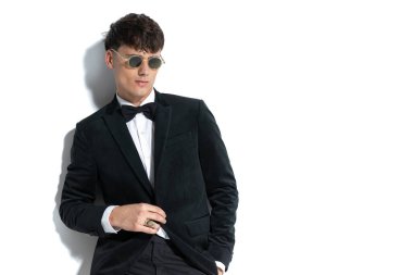 Erkeksi çerçeveli yakışıklı adam ceketini açıyor, yüzük takıyor, güneş gözlüğü takıyor ve elini cebine koyuyor.