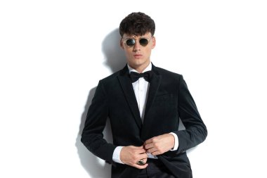 Genç yakışıklı işadamı ceketini kapatıyor, yüzük takıyor ve beyaz stüdyo geçmişine karşı şık poz veriyor.