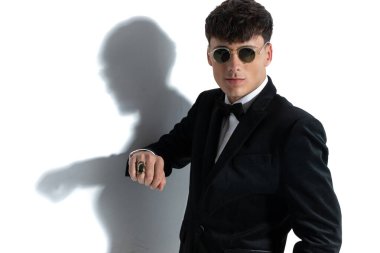 Yakışıklı iş adamı tavır takınıyor, yüzük takıyor, güneş gözlüğü takıyor ve elini cebine koyuyor.