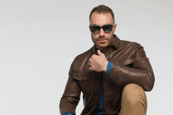 Sexy Casual Man Squatting Wearing Brown Leather Jacket Eyeglasses Gray — стоковое фото
