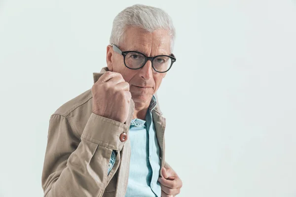 old casual man pulling his jacket\'s collar and wearing eyeglasses in a fashion pose