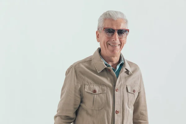 happy casual man smiling at the camera and wearing eyeglasses against gray studio background