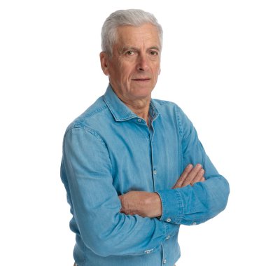 Kot gömlekli, kollarını kavuşturan ve stüdyoda beyaz arka planda poz veren kendinden emin yaşlı bir adamın portresi.