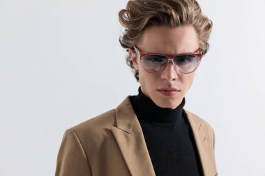 Gözlüklü yakışıklı bir gencin, gri arka planda kendine güvenen şık bir şekilde poz verdiği portresi.