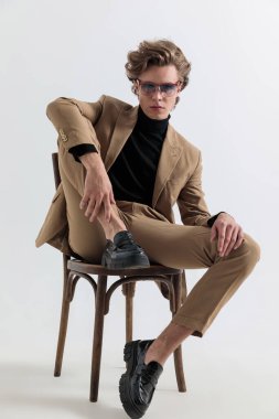 Güneş gözlüklü çekici bir genç. Stüdyodaki gri arka planda diziyle havalı poz veriyor.