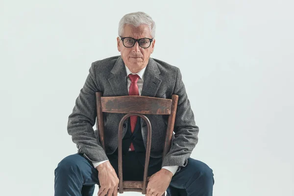 皱眉的商人 灰白的头发 坐在椅子上 背对着灰色的背景 — 图库照片