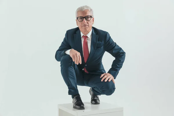 Elegante Velho Empresário Com Óculos Segurando Braços Joelhos Agachado Frente — Fotografia de Stock