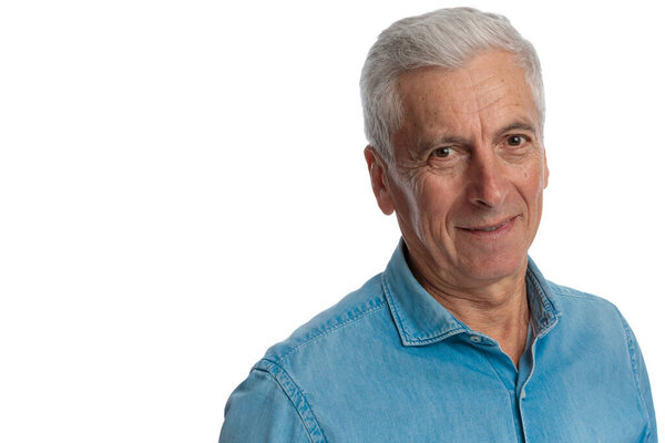 close up picture of grizzled hair man wearing blue jeans shirt and smiling in front of white background in studio