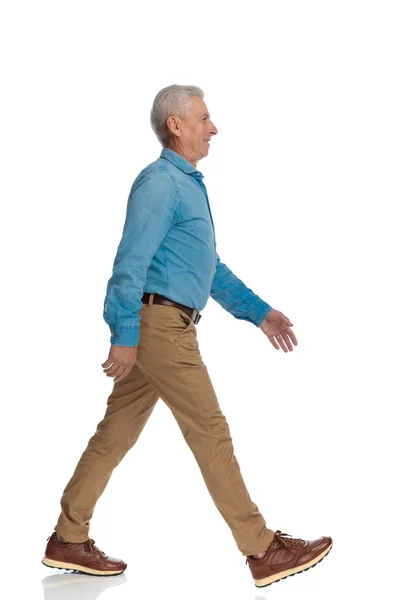スタジオの白い背景の前で自信を持って横を向いて歩いているハンサムな老人のサイドビュー写真 — ストック写真