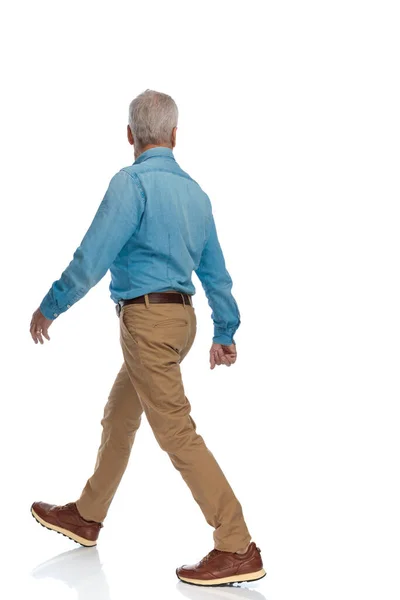 スタジオの白い背景の前を歩いているスニーカー姿のカジュアルな老人の横で — ストック写真
