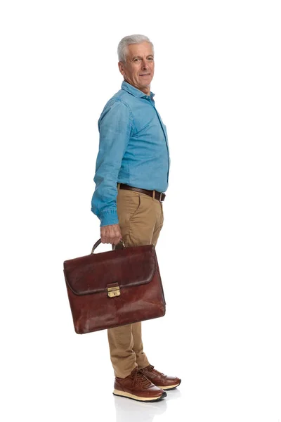 六十多岁的普通老人提着手提箱站在演播室的白色背景前的侧视图 — 图库照片