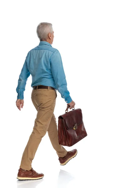 白髪の老人がスーツケースを持ってスタジオで白い背景の前に動く姿を — ストック写真