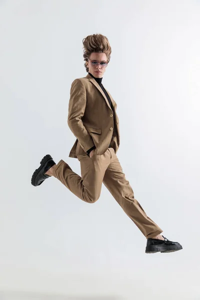 スマートカジュアル男でポケットに手を空中にジャンプし スタジオで灰色の背景の前でポーズ — ストック写真