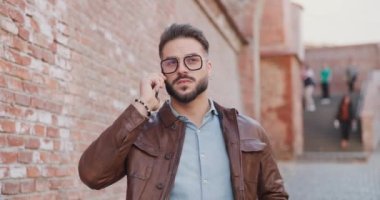 Deri ceketli havalı adam Romanya 'nın ortaçağdan kalma bir kasabasında etrafa bakıp gülerken telefonda konuşuyor.