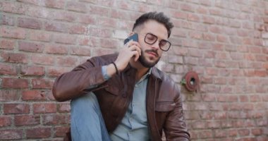 Yakışıklı adamın telefonuna cevap verirken, sohbet ederken, dirseğini dizinde tutarken ve dışarıda otururken çekilmiş bir video.