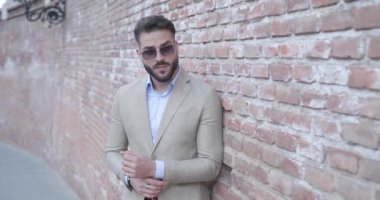 Romanya 'nın ortaçağdan kalma bir kentindeki bir tuğla duvarın kenarına oturup, takım elbise kolları düzenleyen zarif sakallı bir adamın video projesini.