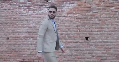Tuğla duvarın önüne atlayan, takım elbise ve güneş gözlüğü takan ve Romanya 'dan gelmiş eski bir kentin arkasına bakan seksi, genç ve şık bir adamın video projesi.