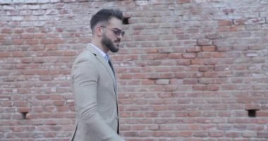 Zarif şık bir adam takım elbise düzenliyor, duvarın önünde yürürken etrafa bakıyor ve Romanya 'nın eski bir kasabasında elleriyle bir silah hareketi yapıyor.