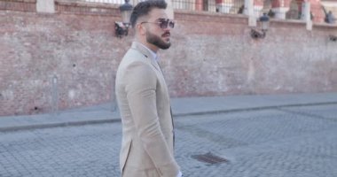 Zarif moda işadamı etrafa bakıyor, avuçlarını ovuyor ve takım elbise ayarlıyor, eski bir şehirde dışarıda yürüyor.