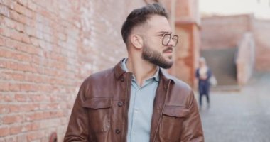 Gözlüklü havalı bir moda adamı etrafa bakıyor, ceketini tamir ediyor, havalı ve kendinden emin, el ele tutuşuyor ve ortaçağ kasabasında kollarını kavuştururken düşünüyor.