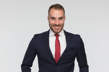 portrait of attractive young businessman in elegant suit with red tie smiling and posing in front of grey background in studio
