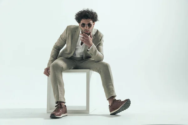 スタジオで灰色の背景の前に座って考えながら膝の上に肘を保持し 顎に触れる思慮深いトルコ人男性 — ストック写真