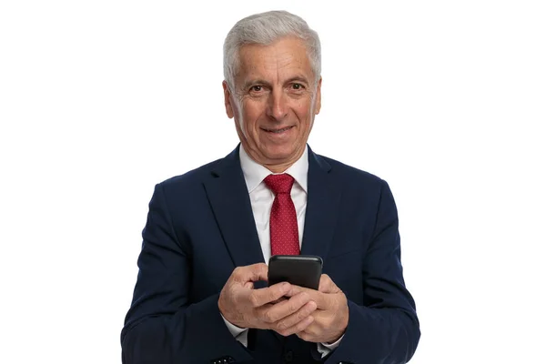 古いビジネスマンは彼の電話でテキストメッセージを送信し 白い背景に笑みを浮かべている — ストック写真