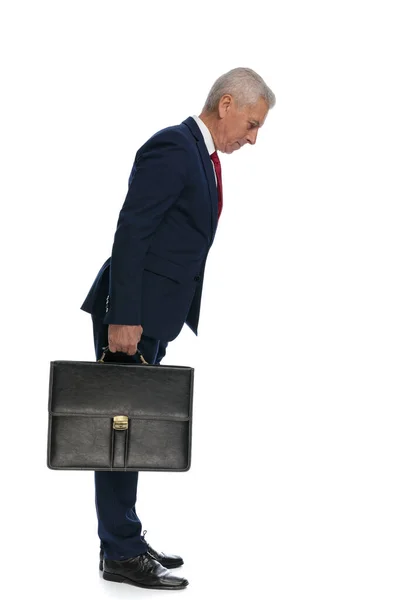 ブリーフケースを持っている間何かをチェックするために傾いている古いビジネスマンの全身像と側面図 — ストック写真