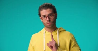 project video of cool fashion man with glasses and curly hair holding finger up and following, pointing finger and indicating on blue background