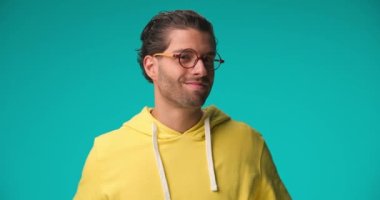happy casual man with curly hair wearing yellow hoodie and glasses having a good time, smiling and laughing on blue background