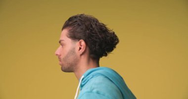 side view of handsome man with long curly hair looking to side, dynamically moving, winking and smiling on yellow background