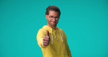 casual Arabic man with curly hair smiling and making thumbs up gesture with hands while laughing and being happy on blue background