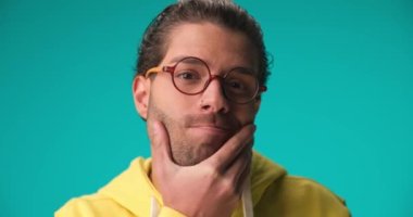 pensive casual Arabic man with glasses touching chin and wondering, scratching head and being confused on blue background