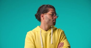 concerned man with curly hair and glasses crossing arms, looking around and thinking, having an idea, smiling and nodding on blue background in studio