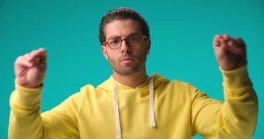 irritated young man with curly hair and glasses holding arms up and making talking hands gestures on blue background